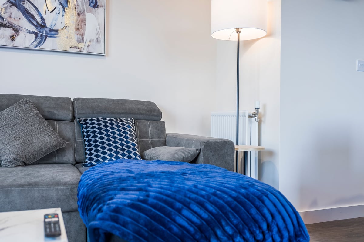 Living room at Wedgewood with a grey upholstered sofa, a blue patterned ottoman, a floor lamp and abstract artwork on the wall