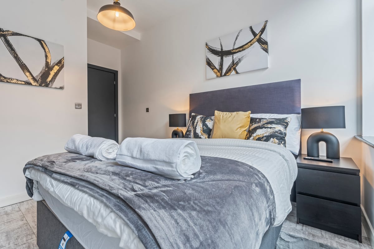 Bedroom at The Calls with black and white bedding, rolled towels and a grey headboard under pendant lighting