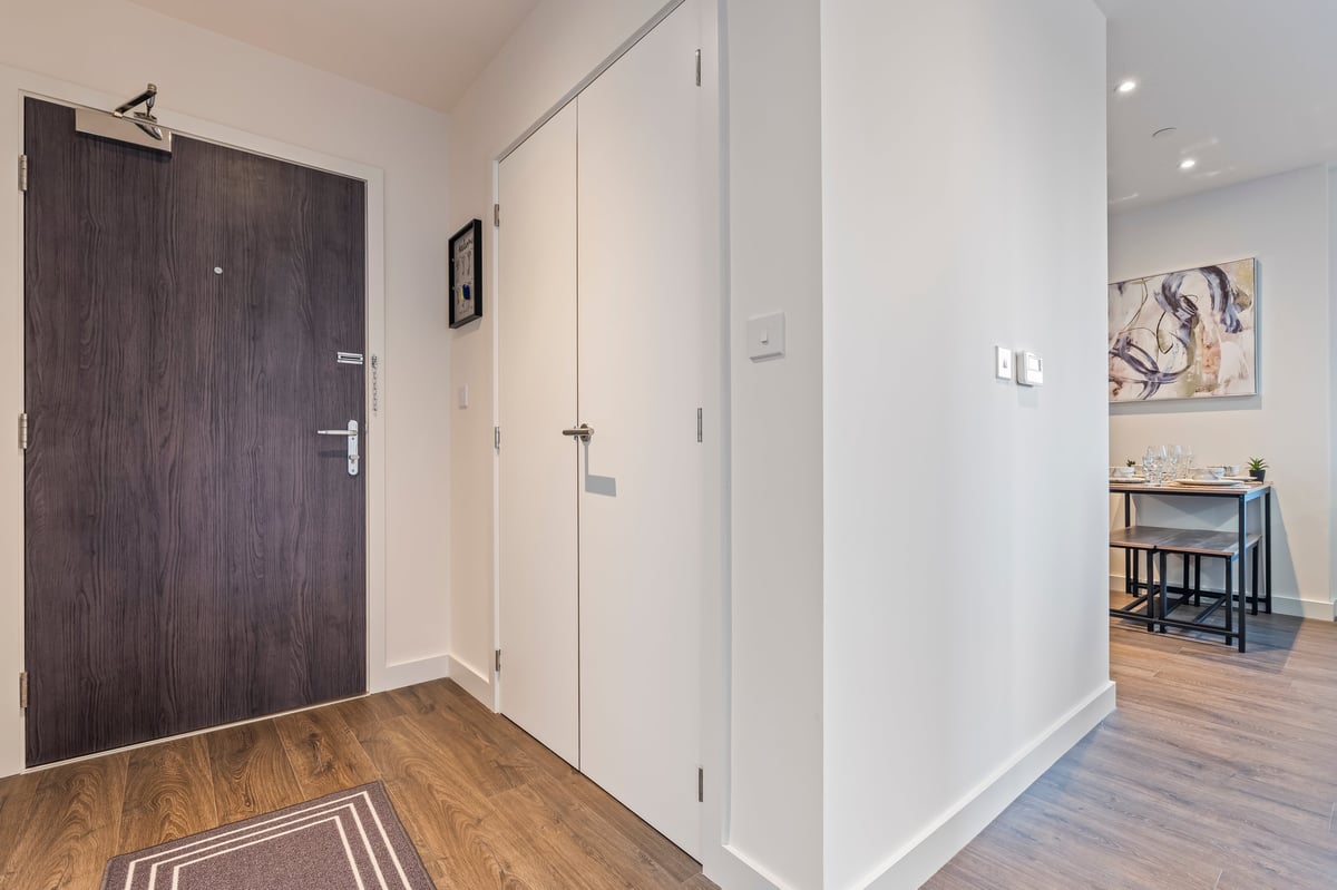 Entryway at Wedgewood with a dark wooden front door, white walls, wooden flooring and a glimpse of the desk and chair in the living space beyond