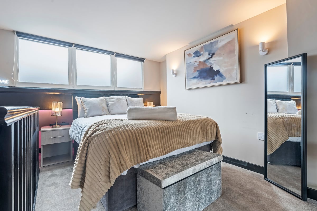The bedroom at Athenaeum House with a made bed and beige throw, bedside lamps, large windows and wall art