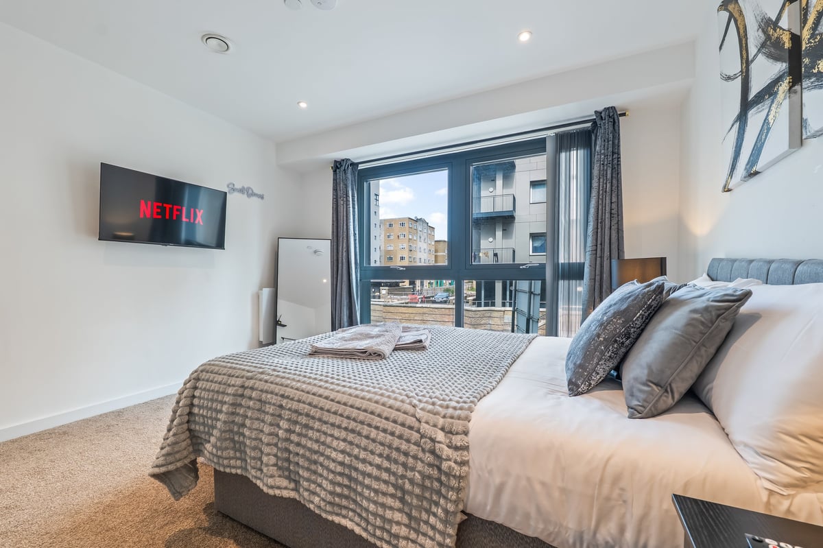 Bedroom at the Aspire apartment with a large bed, wall-mounted television showing Netflix, blue curtains and a city view through floor-to-ceiling windows