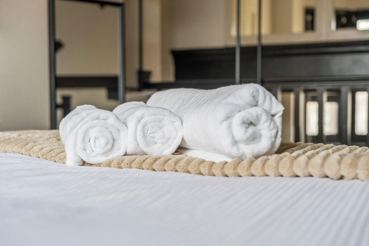 Three rolled white towels arranged on a rope runner on the bed at Athenaeum House with modern bedroom furniture in the background