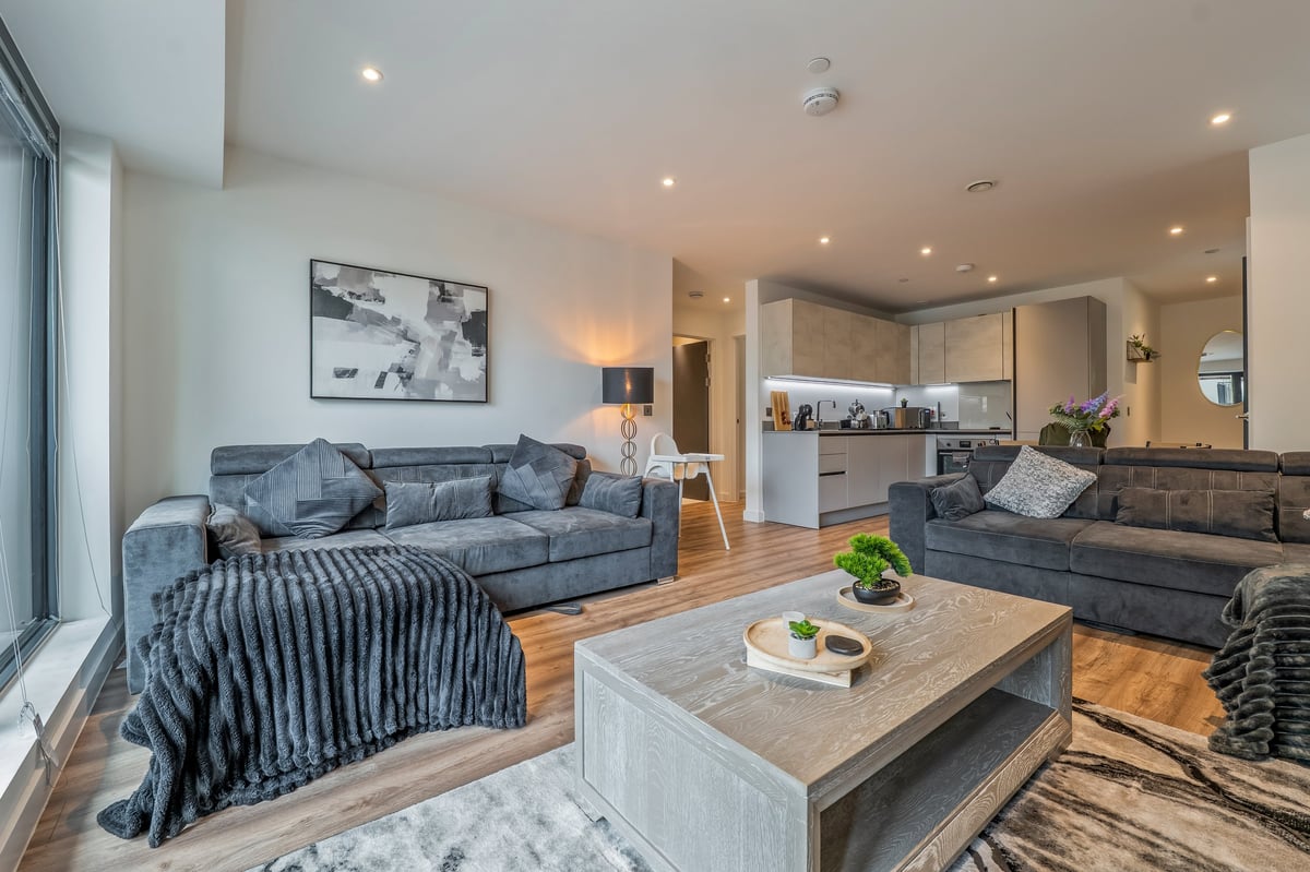 Open-concept living room at the Aspire apartment with two grey sofas, a wooden coffee table, kitchen and hardwood floors