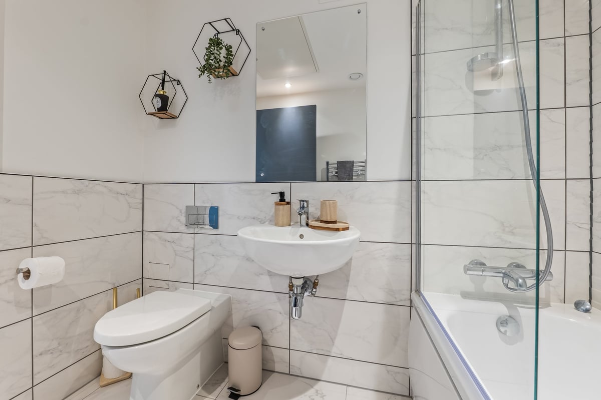 Bathroom at the Aspire apartment with white subway-tiled walls, glass shower enclosure, white sink with mirror, toilet and hanging planters above