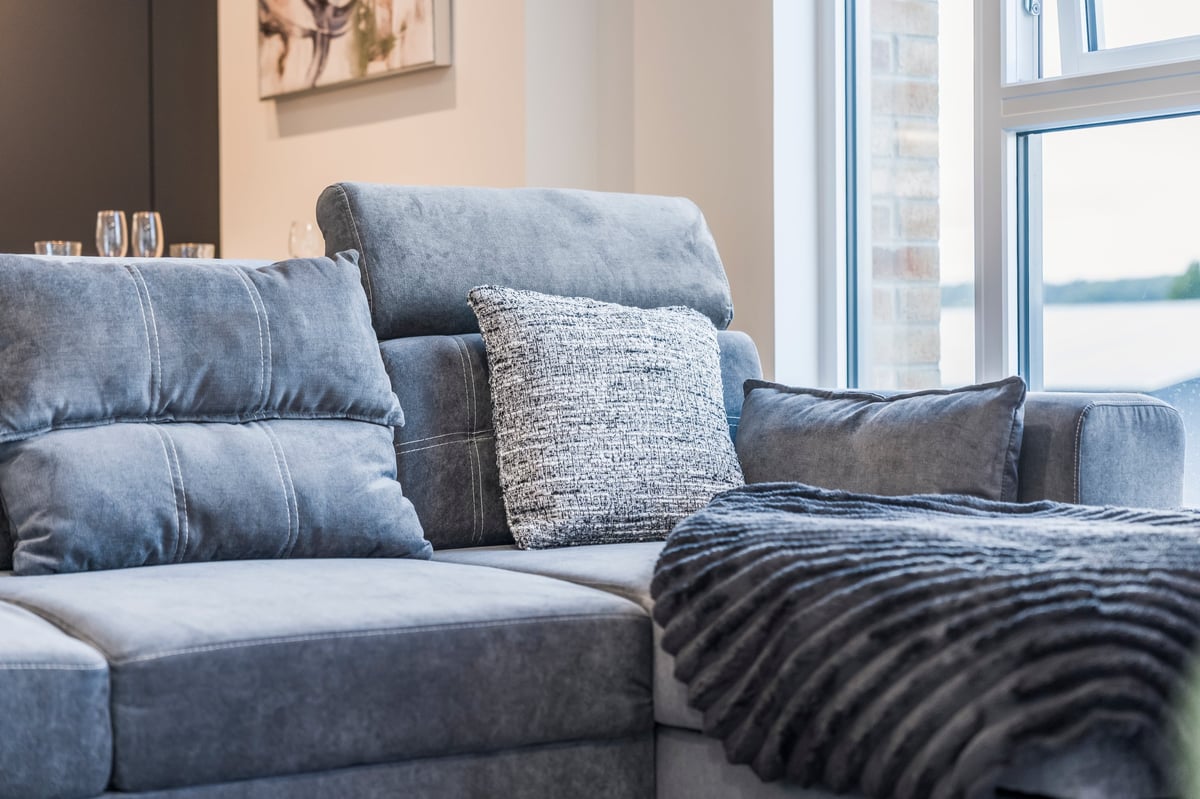 Living room at Wedgewood with a blue upholstered sectional sofa, decorative pillows and a striped throw beside large windows