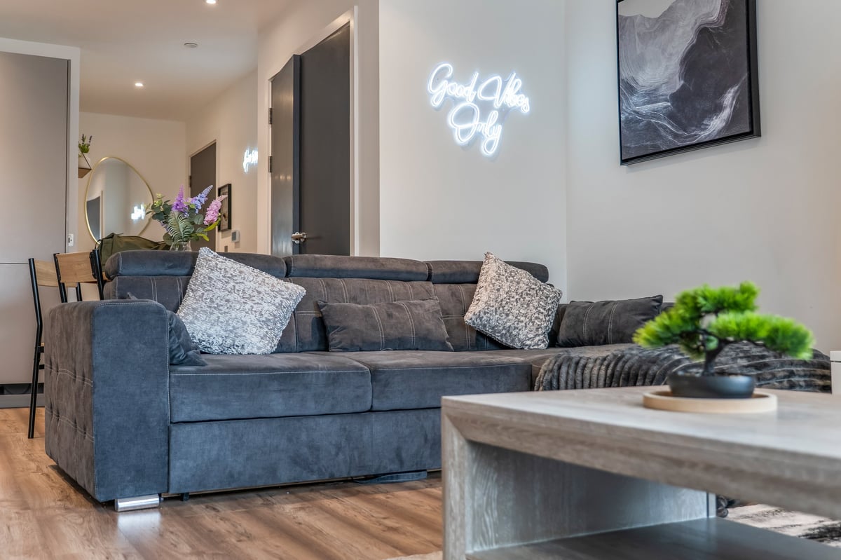 Modern living room at the Aspire apartment with a blue-grey sofa, decorative pillows, neon sign, framed artwork and a wooden coffee table with a potted plant