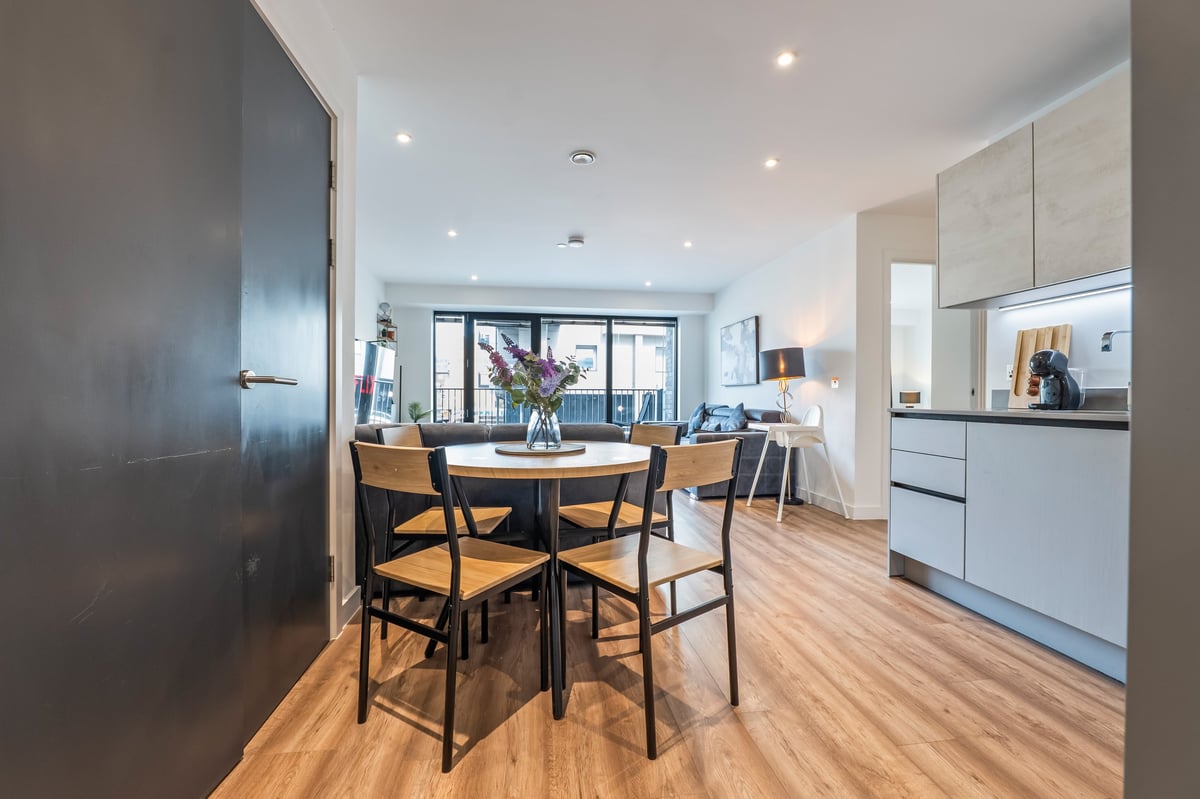 Open-plan kitchen and dining area at the Aspire apartment with wooden flooring, a round black dining table, rattan chairs and white cabinetry