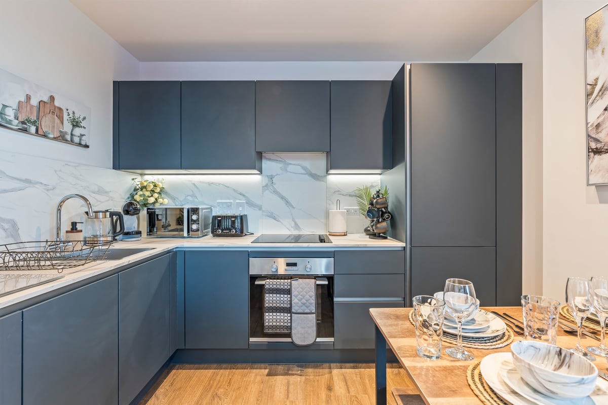 Kitchen at Wedgewood with dark blue cabinetry, marble splashback, a wooden dining table set with place settings and stainless steel appliances