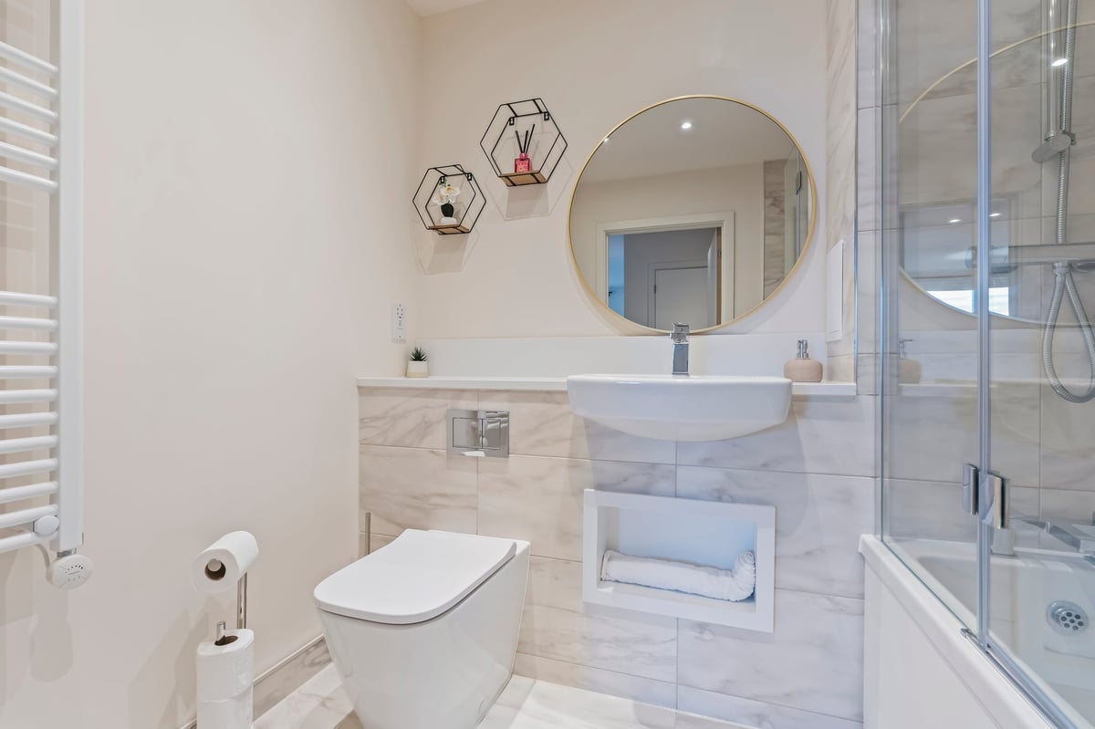 Bathroom at Wedgewood with marble-tiled walls, a round mirror above a floating vanity sink, a white toilet, a glass shower enclosure and decorative hexagonal wall shelves