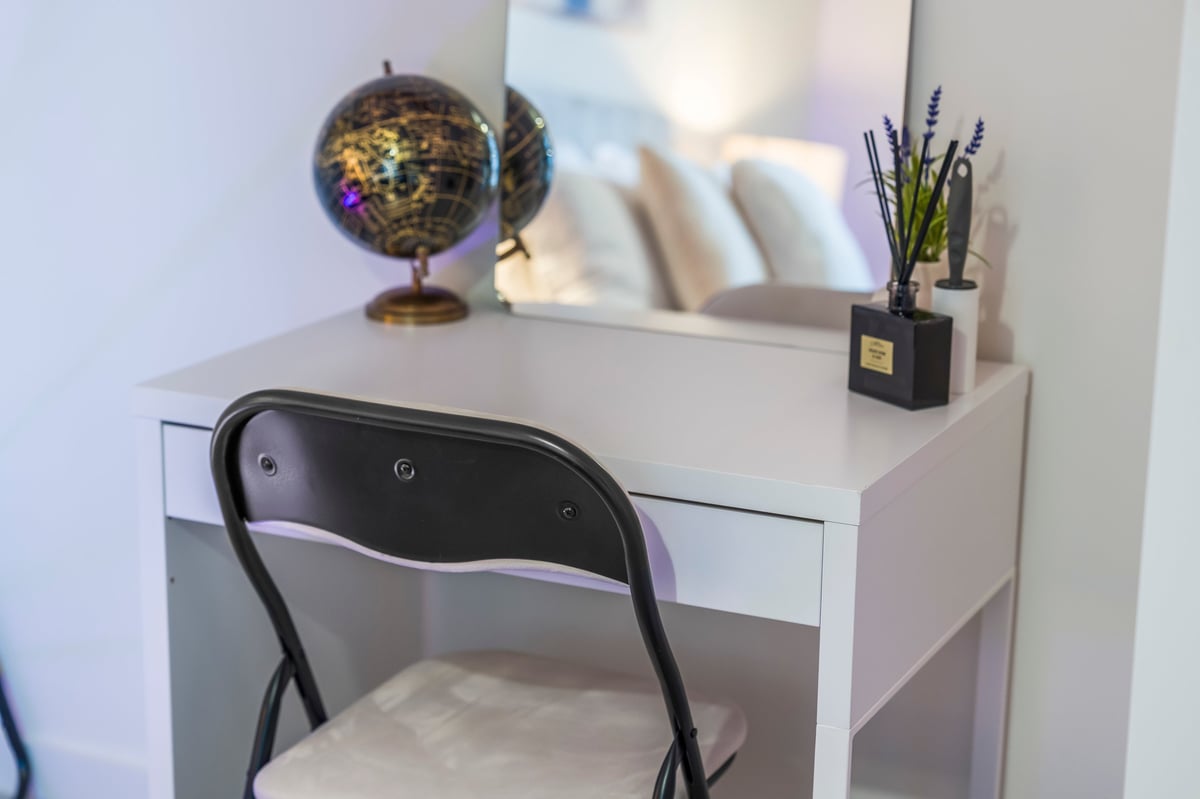 White desk at Wedgewood with a black chair, a decorative gold globe, a small plant and books in a modern minimalist bedroom