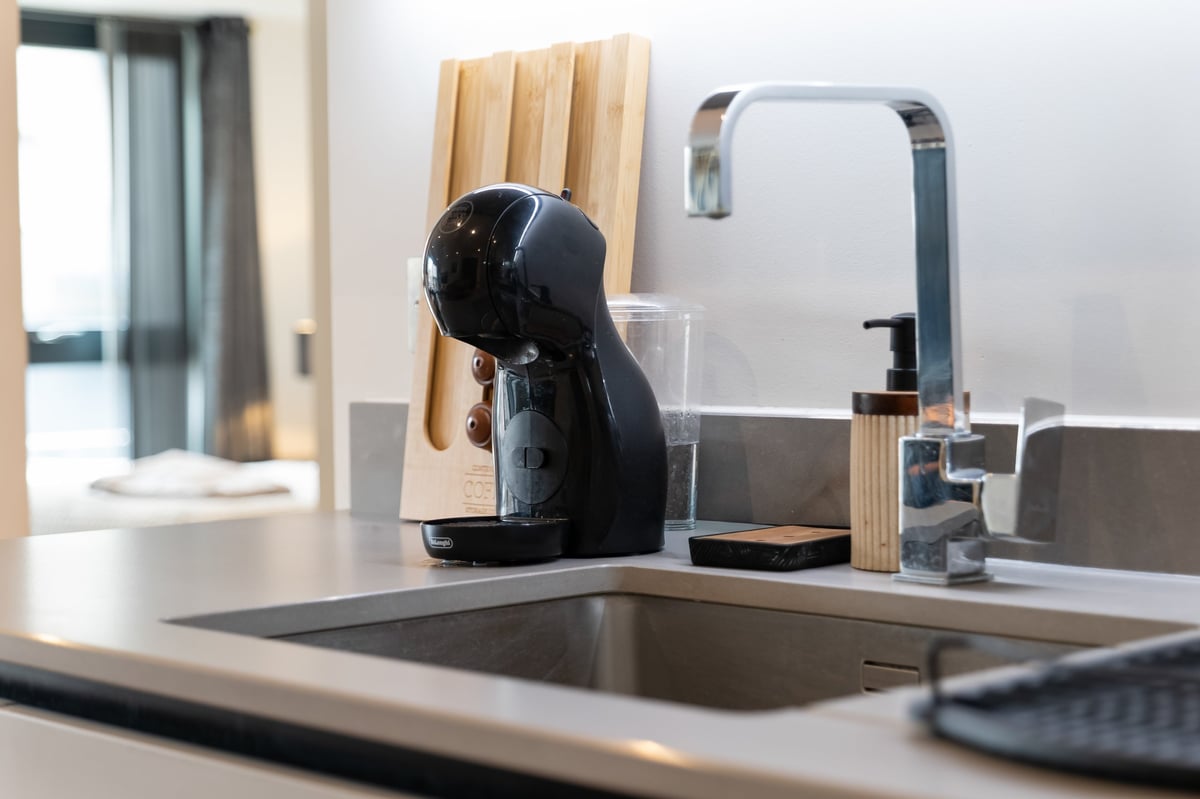 Kitchen counter at the Aspire apartment with a black coffee machine, wooden knife block, chopping boards and a stainless steel sink and mixer tap