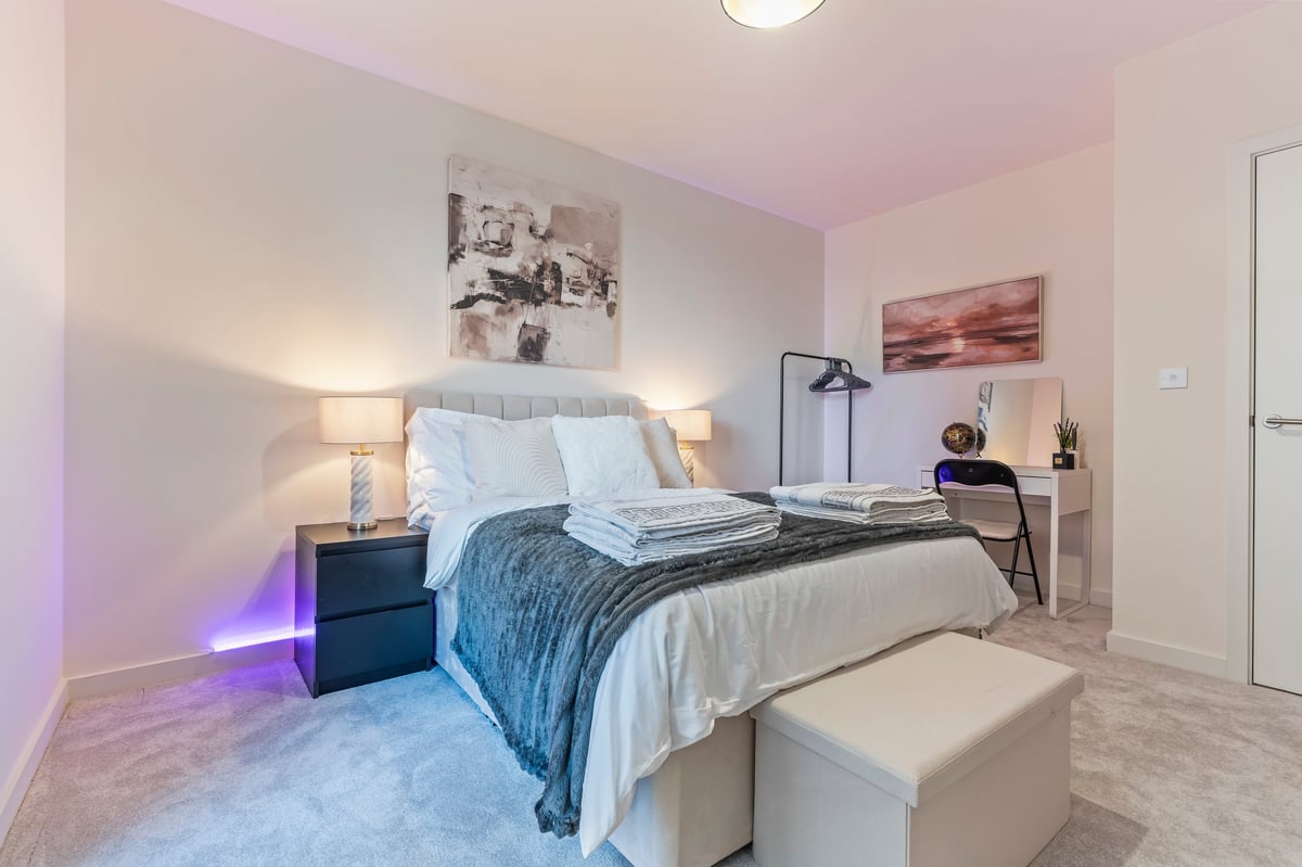 Bedroom at Wedgewood with a queen bed, blue bedding, nightstands with lamps and a desk in soft pink and warm tones