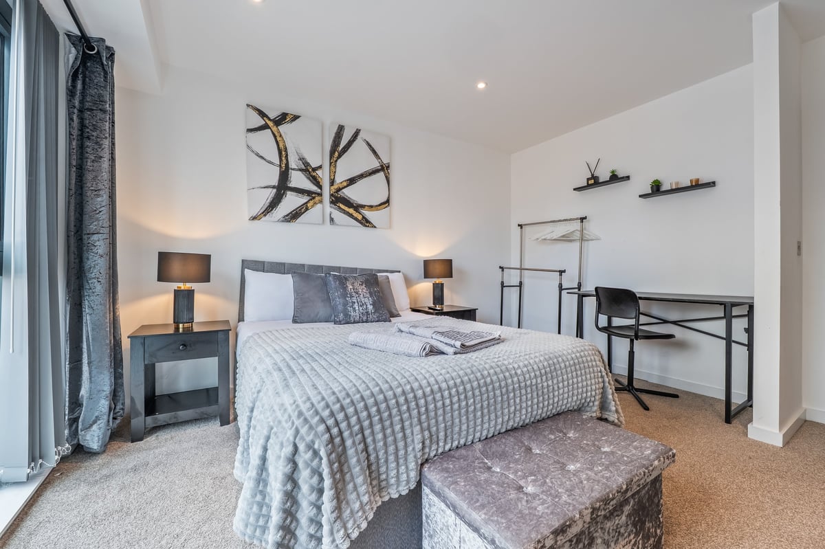Bedroom at the Aspire apartment with a queen bed, nightstands with lamps, wall art, a work desk and contemporary decor in neutral tones