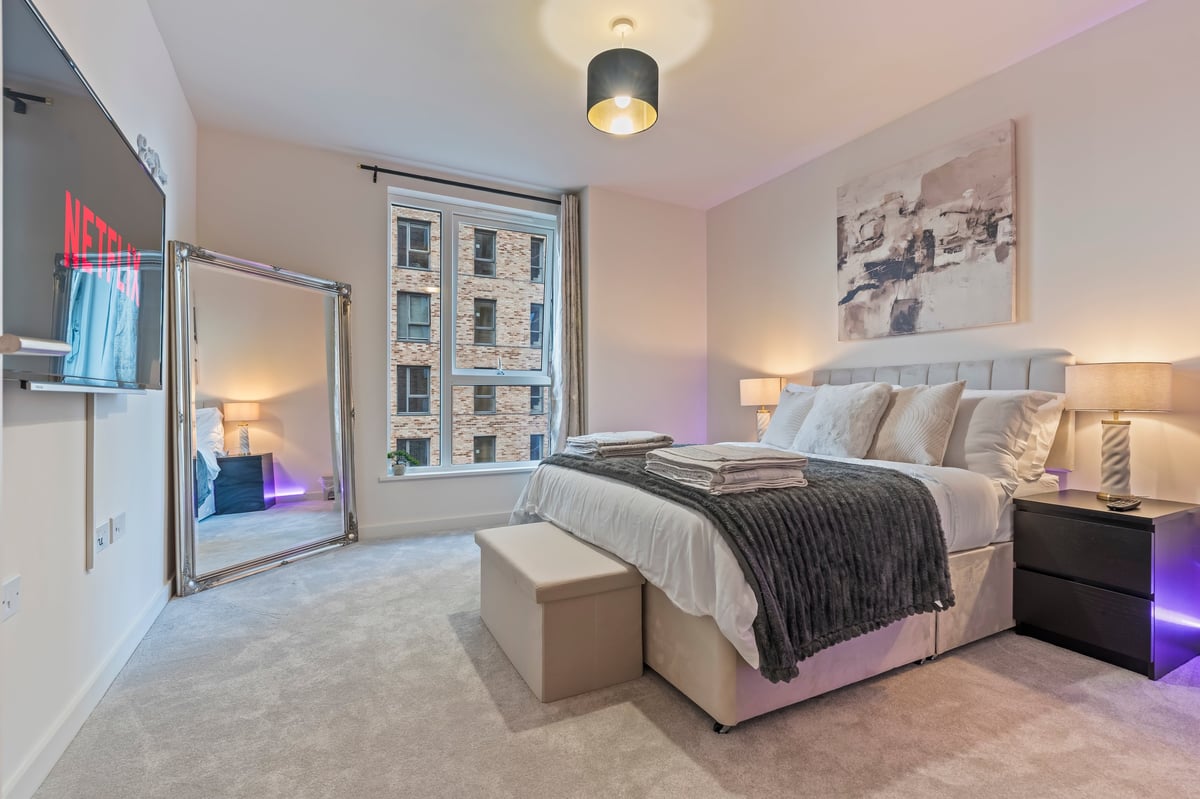Bedroom at Wedgewood with a queen bed, grey upholstered headboard, mirrored wardrobe, large windows and abstract artwork over the bed