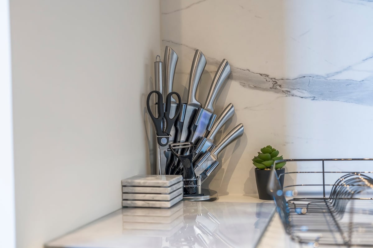 Kitchen counter at Wedgewood with a stainless steel knife block, stacked cookbooks, a potted plant and abstract artwork
