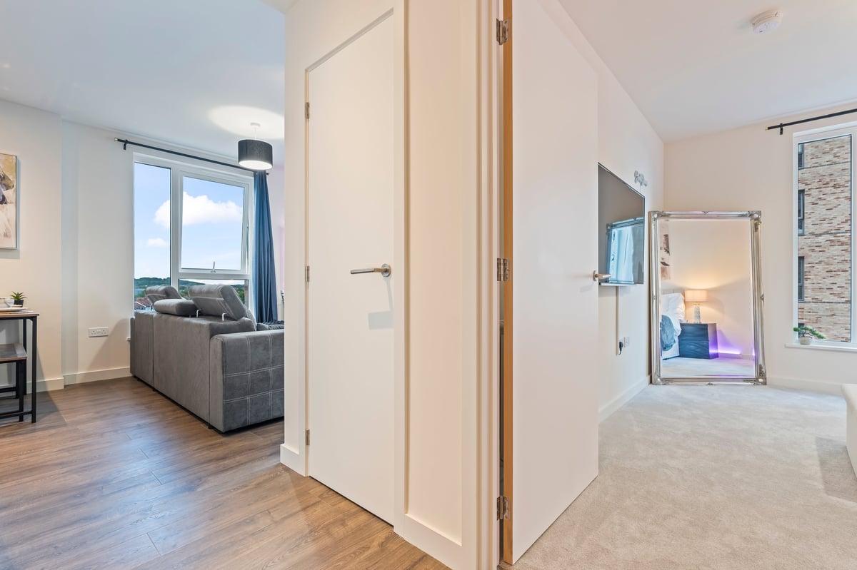 View from the hallway at Wedgewood looking through open doorways into the open-plan living area with hardwood flooring, white walls and contemporary furnishings