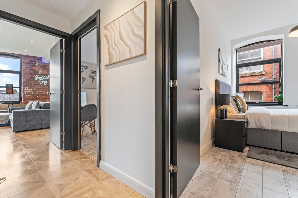 Open-plan living space at The Calls with black-framed glass partition doors, herringbone flooring and exposed brick