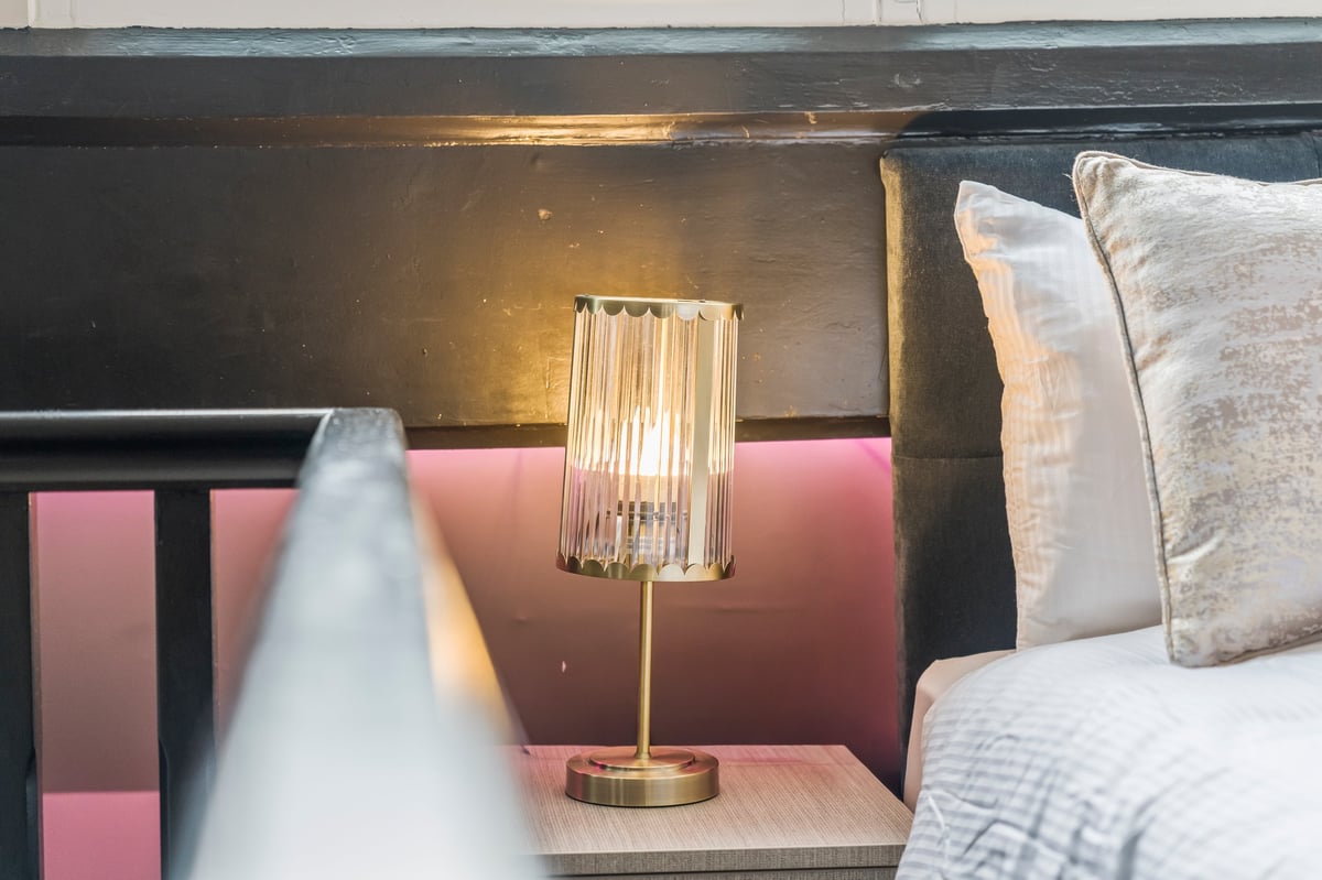 Modern bedroom nightstand with a crystal table lamp, white pillows, a pink headboard and warm evening light through the window at Athenaeum House