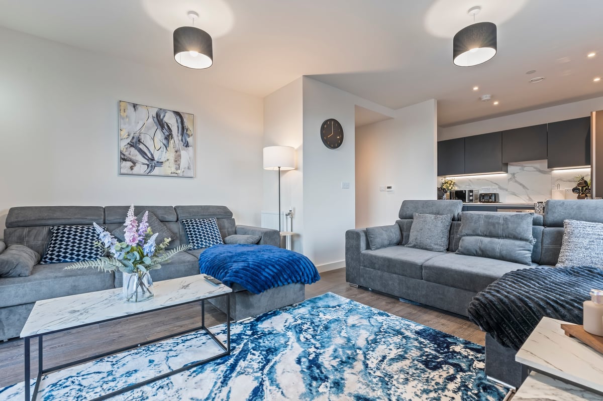 Open-plan living room at Wedgewood with grey sofas, a blue abstract rug, a marble coffee table and pendant lighting