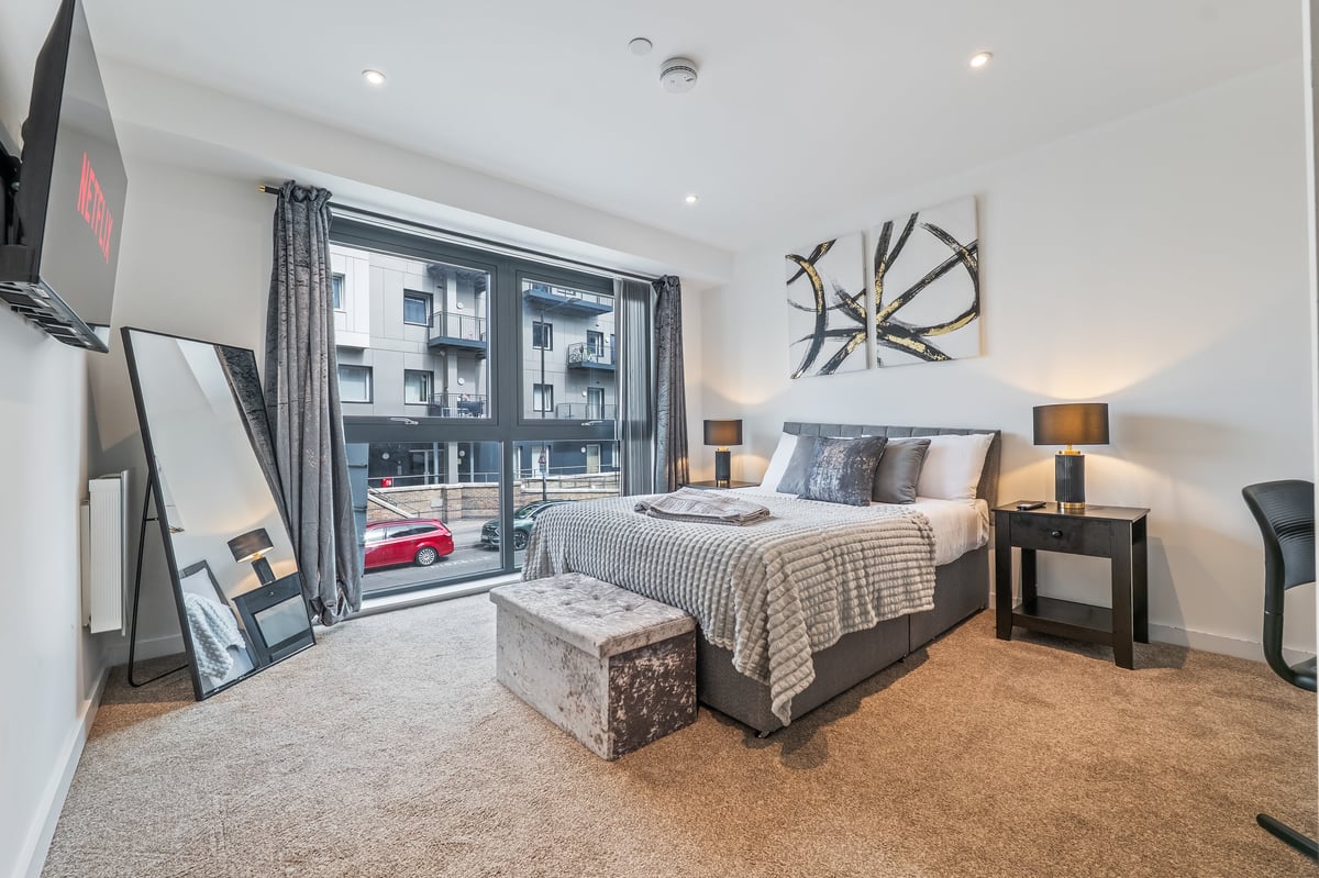Bedroom at the Aspire apartment with a striped bedspread, nightstands, wall art and floor-to-ceiling windows overlooking a city view