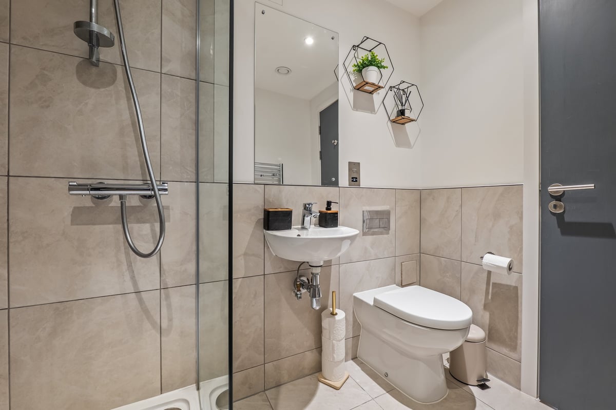 Bathroom at the Aspire apartment with a tiled shower, wall-mounted sink, white toilet and hanging plant decorations
