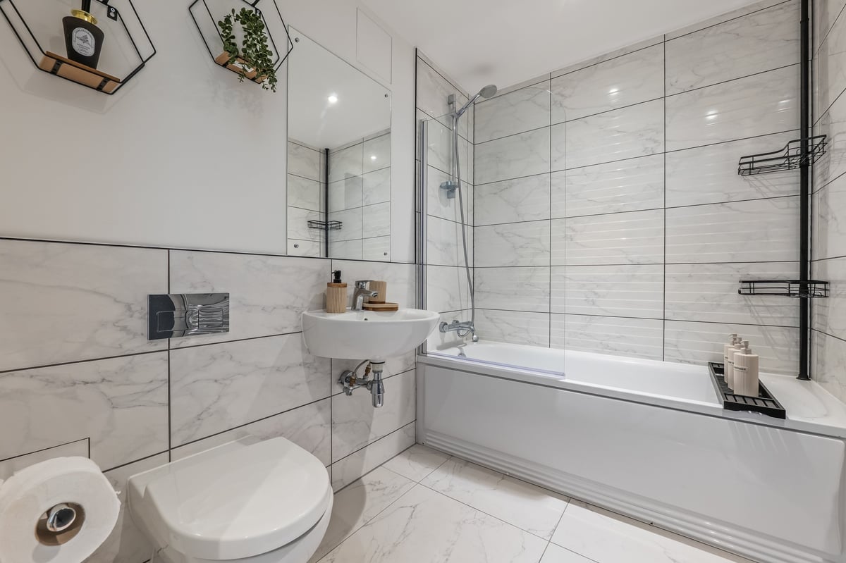Bathroom at the Aspire apartment with white subway tile, toilet, wall-mounted sink, glass shower enclosure and a white bathtub with chrome fittings
