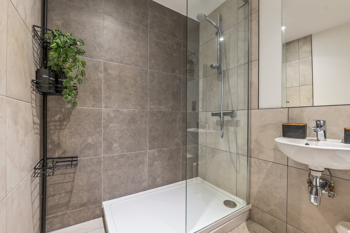 Bathroom at the Aspire apartment with a walk-in shower behind glass doors, a white shower base, grey tiled walls and a sink with mirror