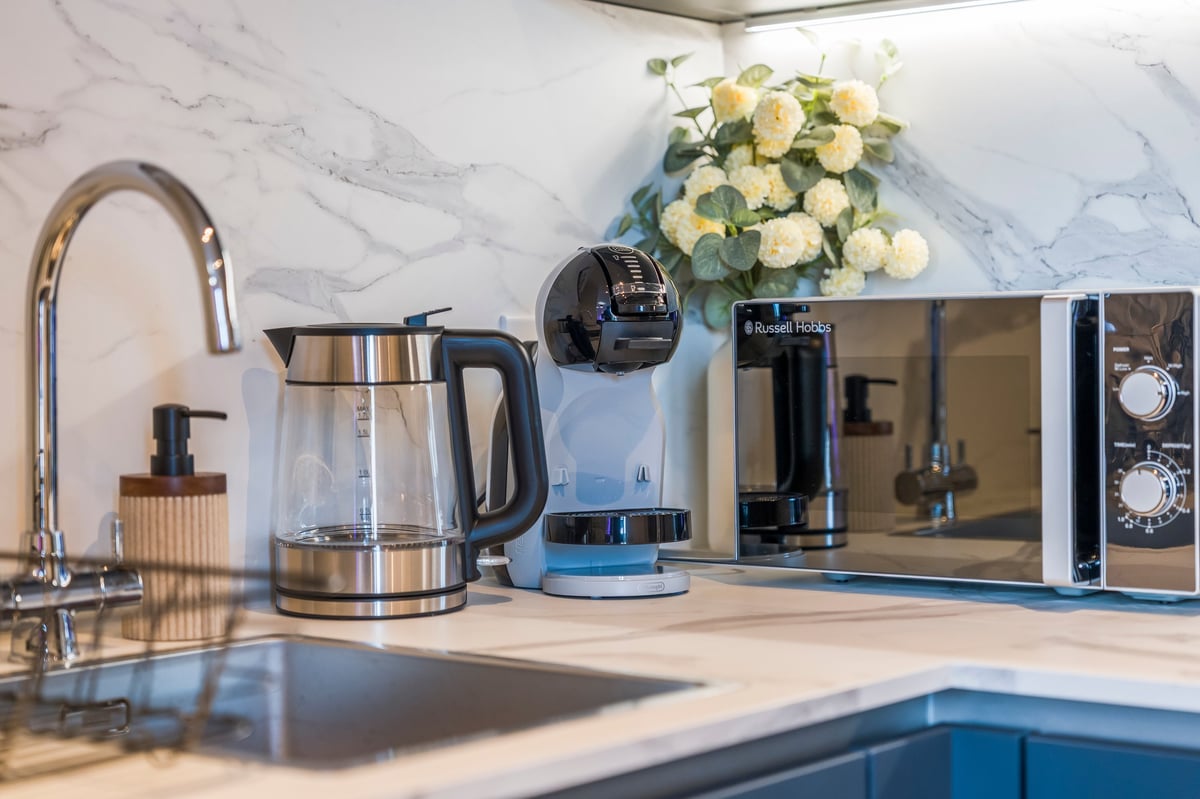 Kitchen countertop at Wedgewood with a stainless steel kettle, a coffee maker, a microwave and fresh flowers against a marble splashback