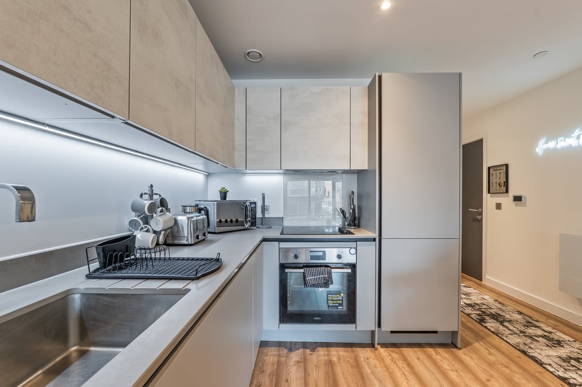 Kitchen at the Aspire apartment with light wood cabinets, stainless steel appliances, white splashback and wooden flooring