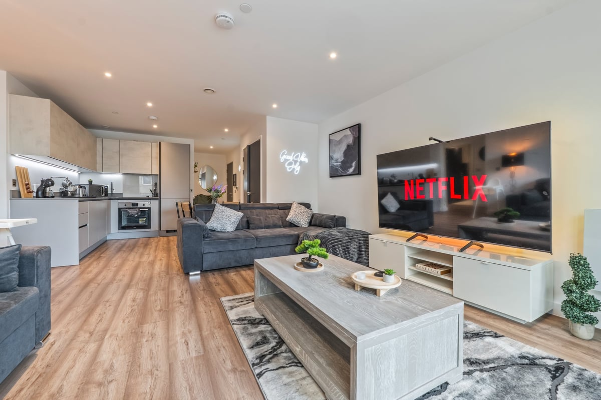 Open-plan living room and kitchen at the Aspire apartment with a grey sofa, wall-mounted television displaying Netflix, wooden flooring and contemporary furnishings