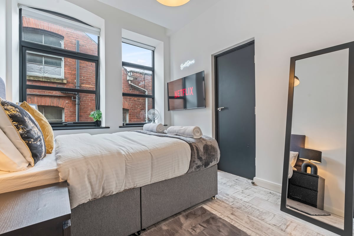 Second bedroom at The Calls with a grey bed, gold cushions, a floor mirror and large windows