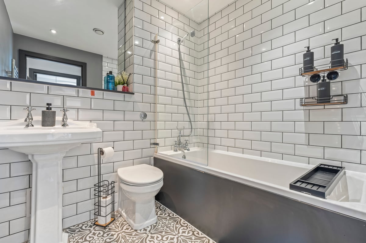 Bathroom at The Calls with white subway tiling, a pedestal sink and pendant lights above the bath