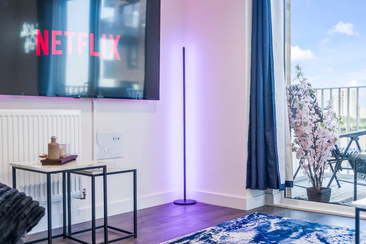 Living room at Wedgewood with Netflix on the wall-mounted television, purple ambient lighting, a blue patterned rug and floor-to-ceiling windows