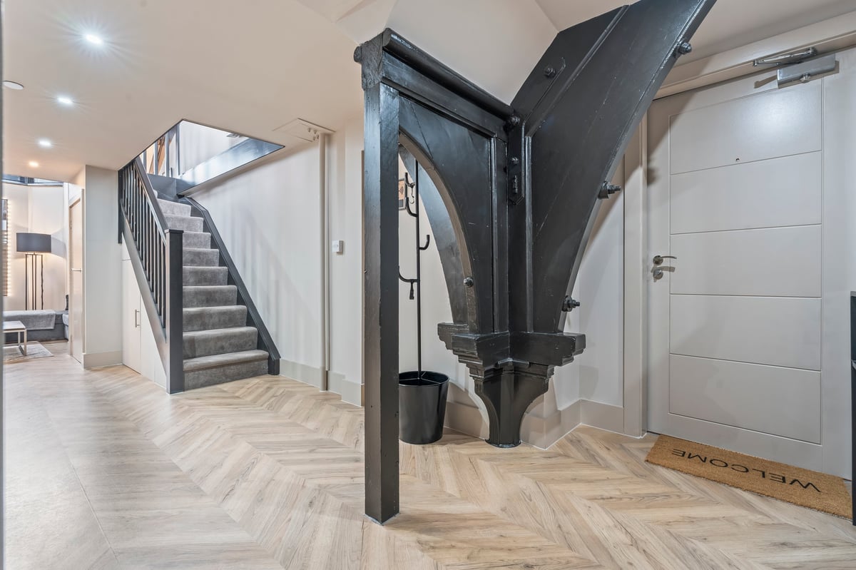Modern entryway at Athenaeum House with herringbone wood flooring, a black steel staircase, white doors and a sculptural black metal art installation