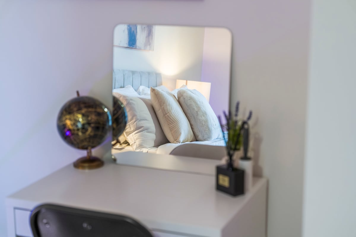 Bedroom vanity at Wedgewood with a mirror reflecting pillows on a bed, a decorative globe and a small plant