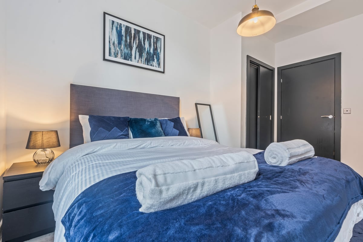 Bedroom at The Calls with blue bedding, a grey headboard, rolled white towels and pendant lighting