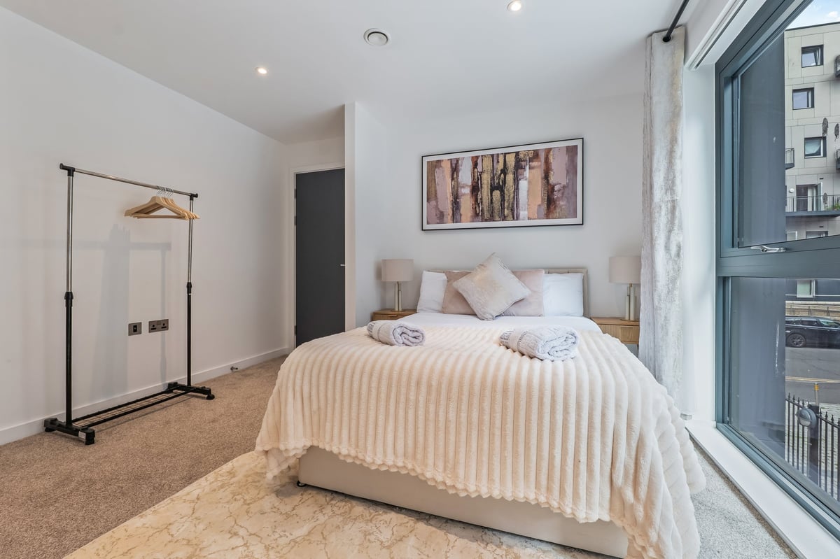 Minimalist bedroom at the Aspire apartment with white quilted bedding, a cream carpet and a large window overlooking city buildings