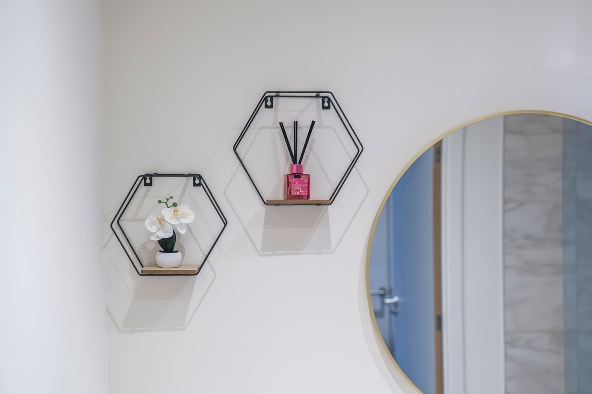 Two hexagonal wall-mounted shelves with decorative items above a round mirror with a blue frame at Wedgewood