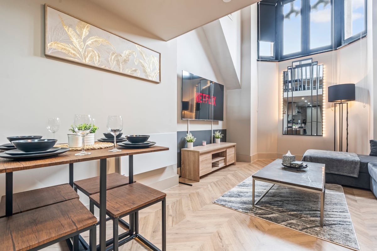 Modern open-concept loft at Athenaeum House with the dining table, kitchen area, living room with grey sofa and large windows