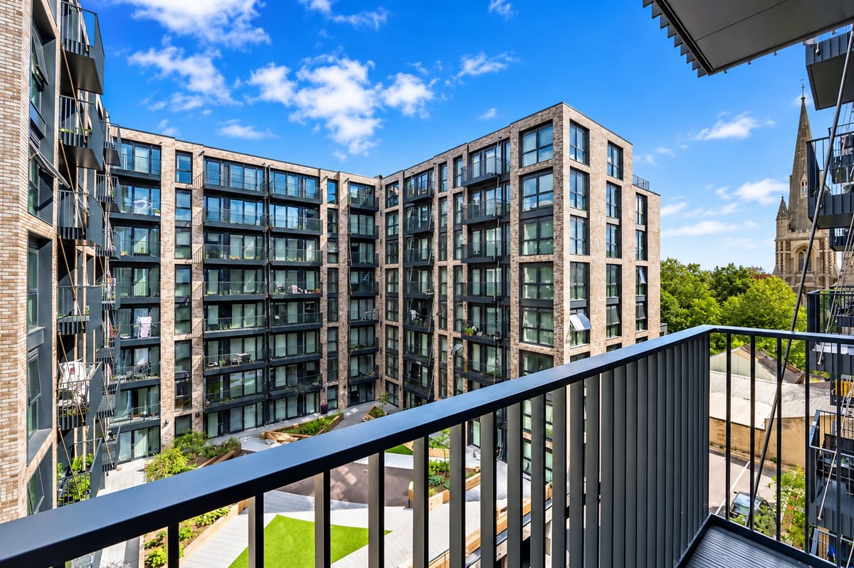 View from a modern apartment balcony overlooking a residential complex with contemporary multi-story buildings under blue sky