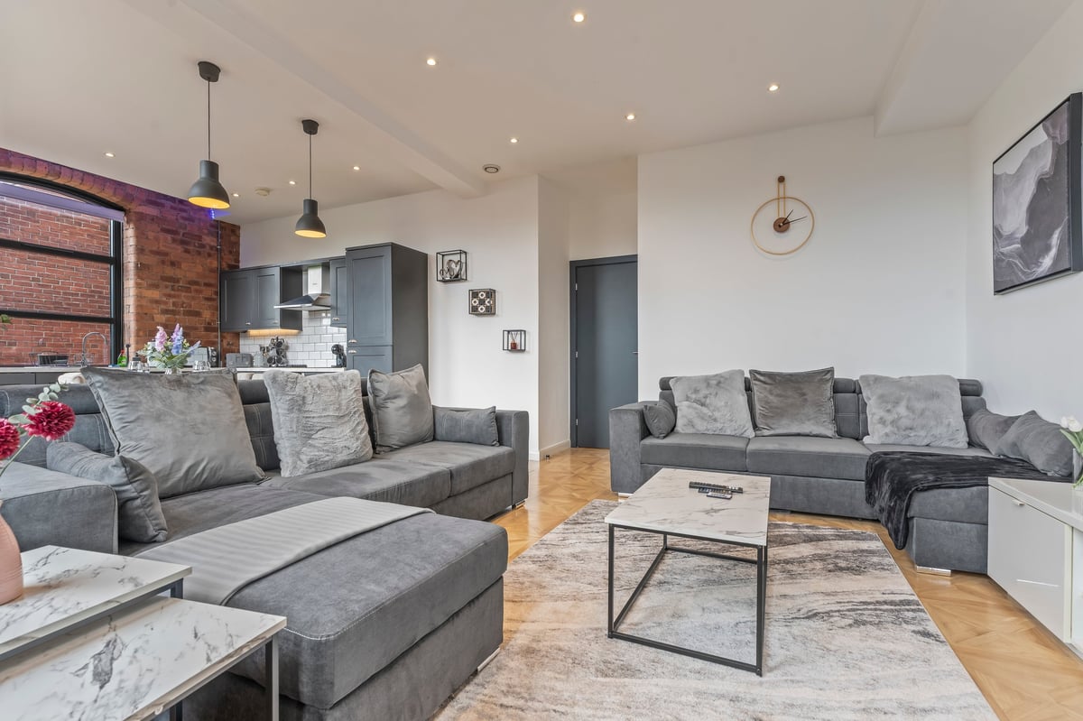 Living room at The Calls with a grey sectional sofa, marble coffee table and exposed brick wall
