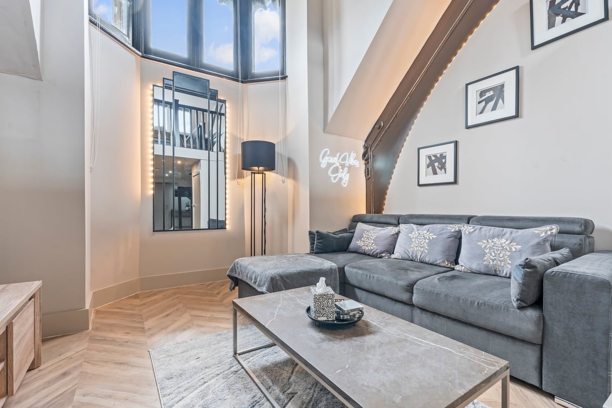 Loft living room at Athenaeum House with a grey sectional sofa, marble coffee table, herringbone flooring and exposed wooden beams