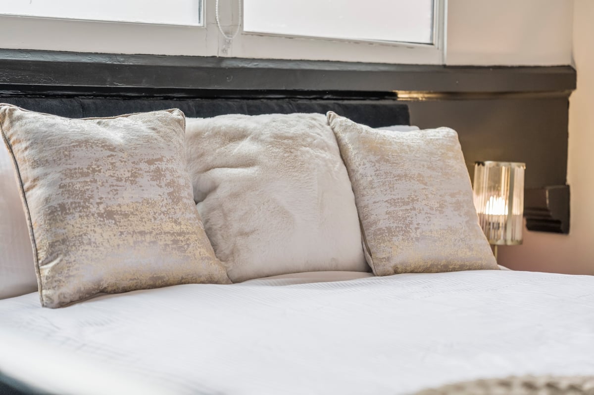 Bed with white sheets and three decorative beige and tan pillows arranged against a black headboard at Athenaeum House