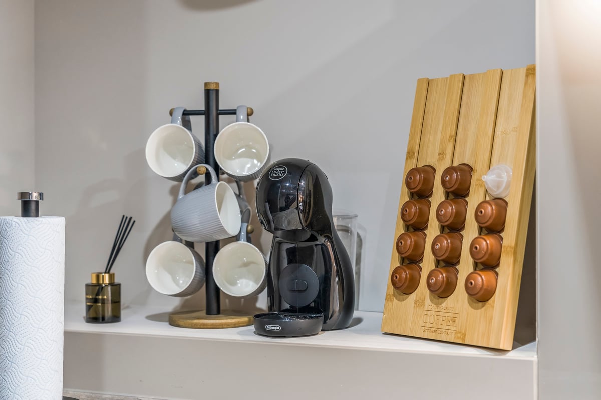Kitchen shelf at Athenaeum House holding a mug set on a stand, a coffee maker and a wooden donut holder