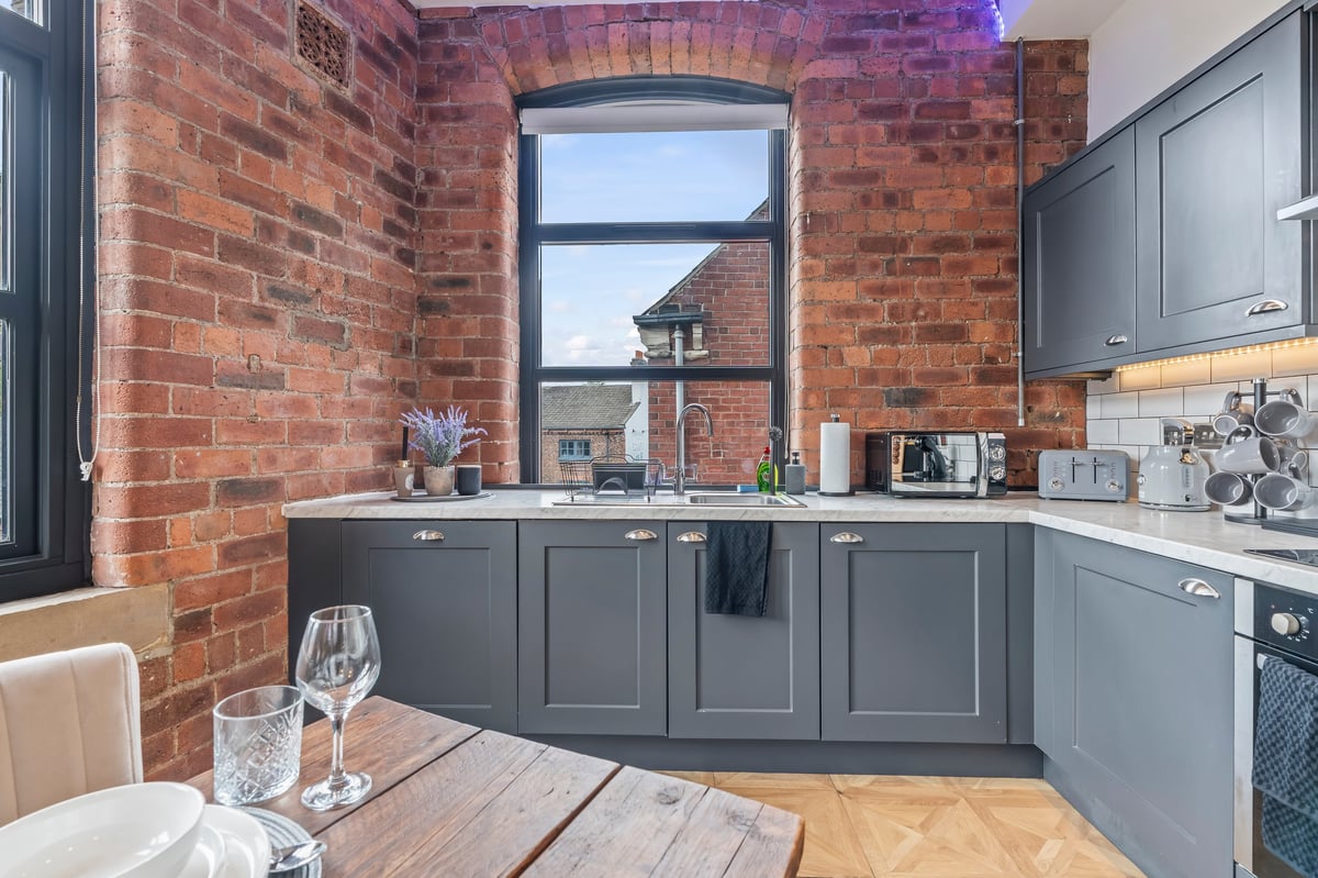 Kitchen at The Calls with grey cabinetry and exposed brick, a large window over the dining table