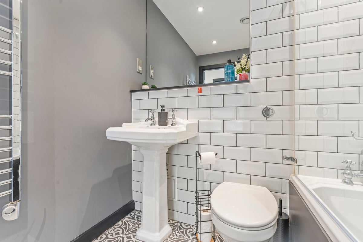 Second bathroom at The Calls with white subway tiling, a pedestal sink and a bath with patterned flooring