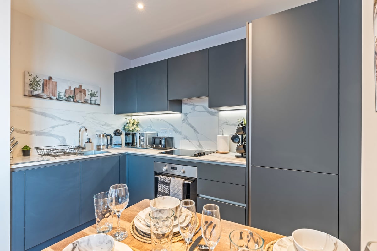 Kitchen at Wedgewood with blue and grey cabinetry, a marble splashback and a dining table set with place settings in the foreground