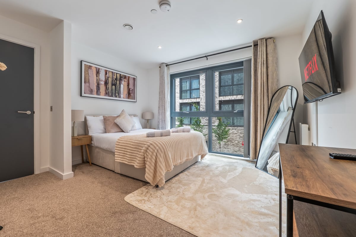 Bedroom at the Aspire apartment with a bed, mounted television, desk and balcony doors overlooking the cityscape