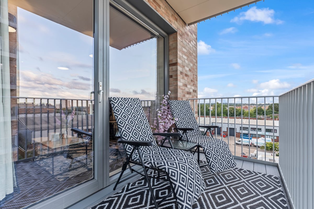 Balcony at Wedgewood with patterned flooring, two black chairs and a city view through the open glass door under a blue sky