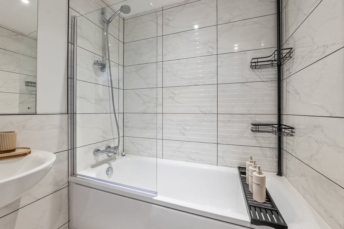 Bathroom at the Aspire apartment with white marble tiles, glass shower enclosure over a white bathtub, rainfall showerhead and chrome fittings